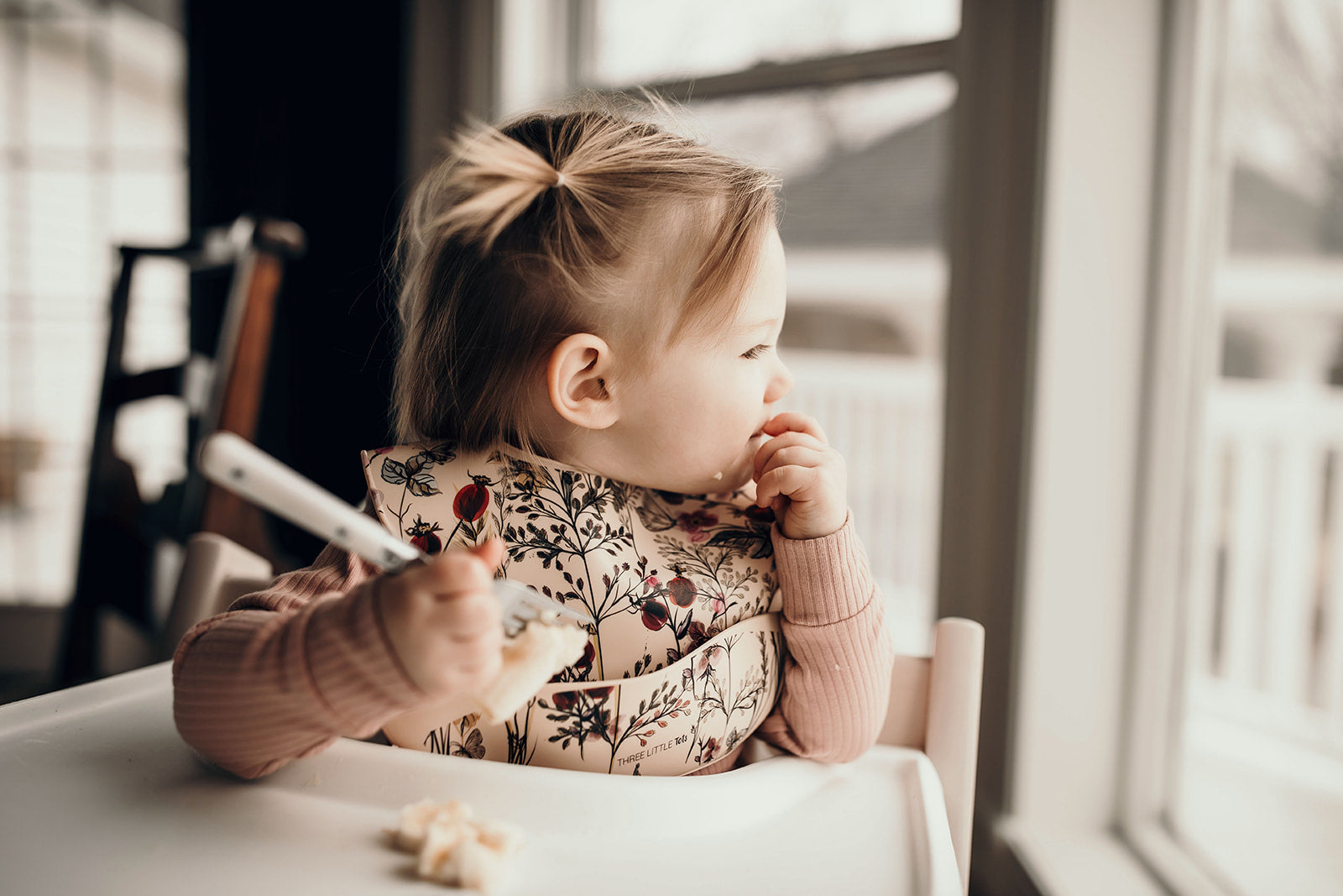 Little girl eating mashed bananas with a Three Little Tots floral silicone bib