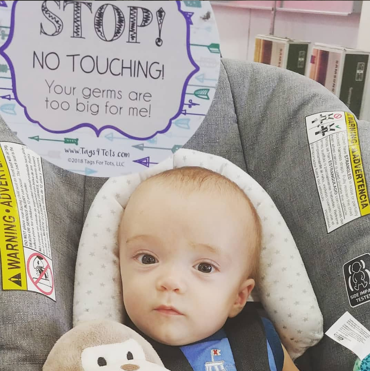 Newborn baby in a car seat with a Three Little Tots No touching baby Car Seat Sign