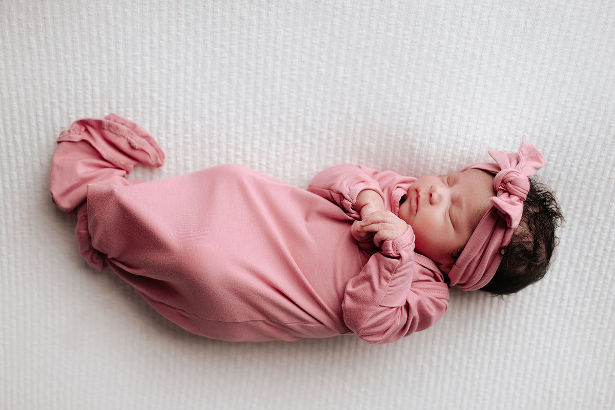 Luxuriously soft modal knotted baby gowns for newborn babies, offering comfort, easy diaper changes, and style. Three Little Tots Rose Pink Knotted baby gown in a Plum and Sparrow Moses basket with a snuggl me organic