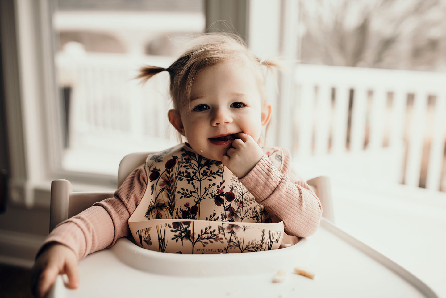 Little girl eating with a Three Little Tots floral silicone bib