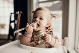 Little girl eating smashed bananas with a Three Little Tots floral silicone bib