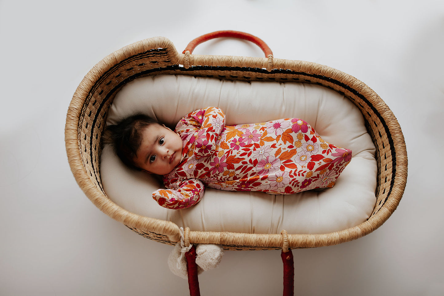  Newborn baby girl in a Floral Three Little Tots knotted gown. Laying in a Snuggle Me organics in a Plum and Sparrow Moses Basket