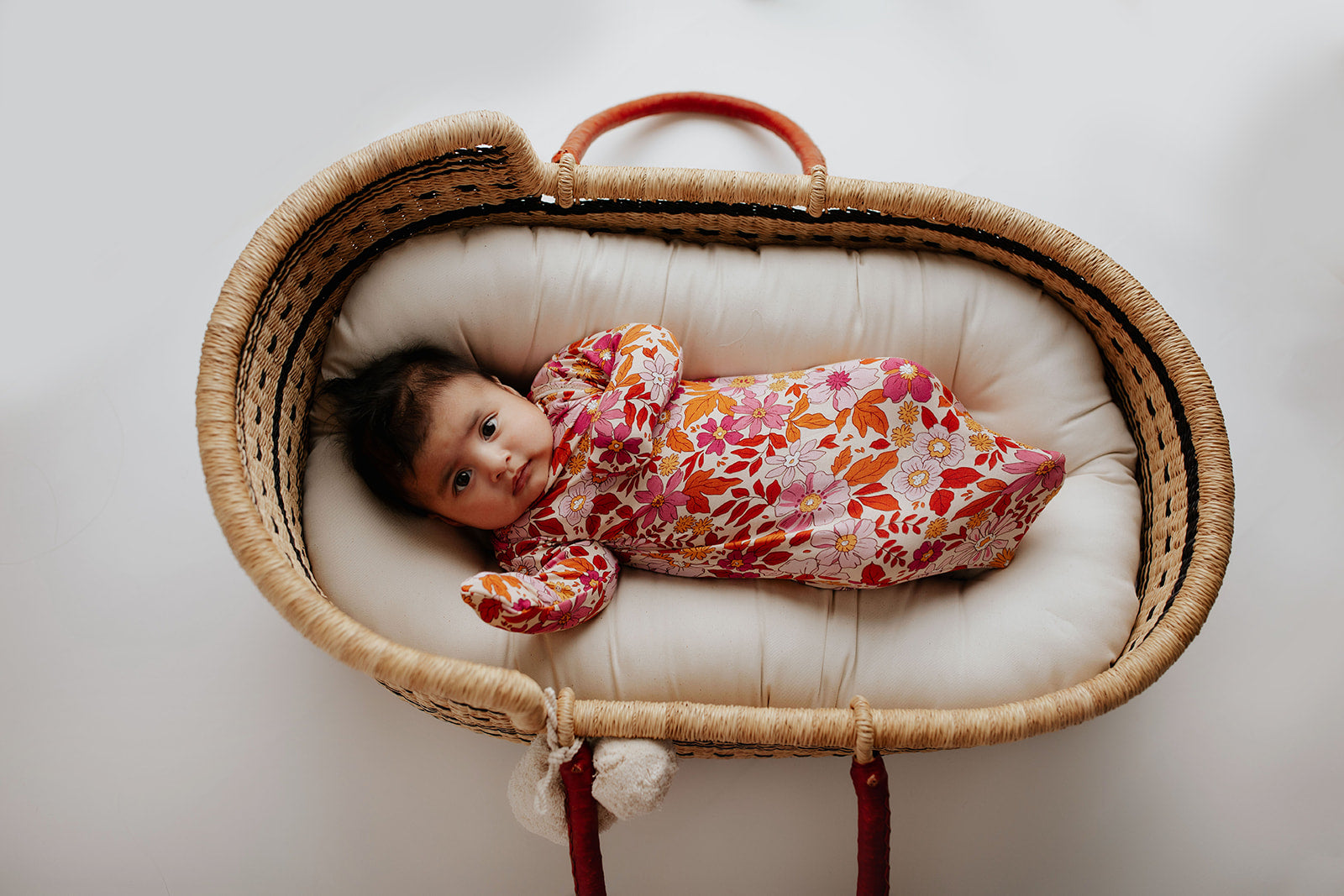  Newborn baby girl in a Floral Three Little Tots knotted gown. Laying in a Snuggle Me organics in a Plum and Sparrow Moses Basket