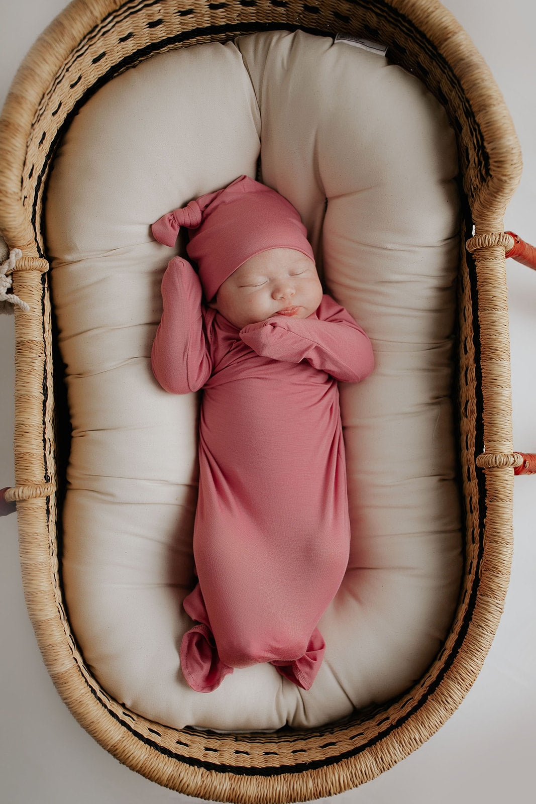 Luxuriously soft modal knotted baby gowns for newborn babies, offering comfort, easy diaper changes, and style. Three Little Tots Rose Pink Knotted baby gown in a Plum and Sparrow Moses basket with a snuggl me organic