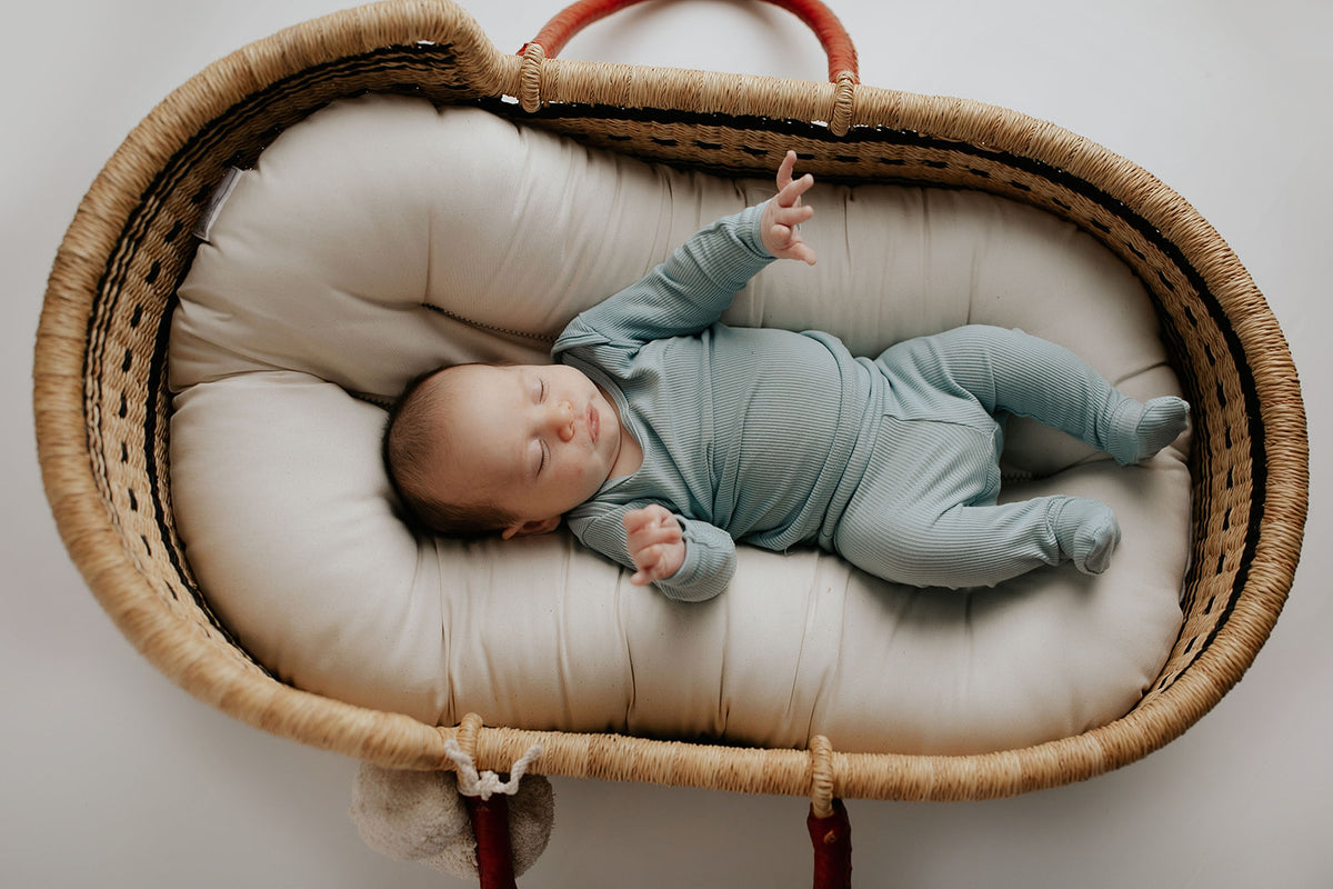 newborn baby in three little tots pajamas in the plum + sparrow moses baby basket