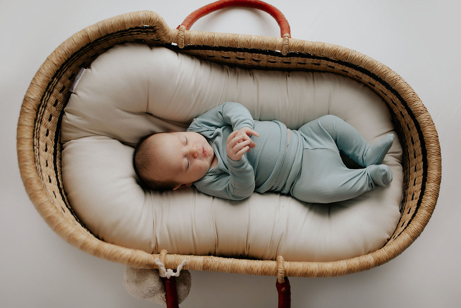 newborn baby in Three Little Tots Pajamas in a Plum + Sparrow Moses Basket