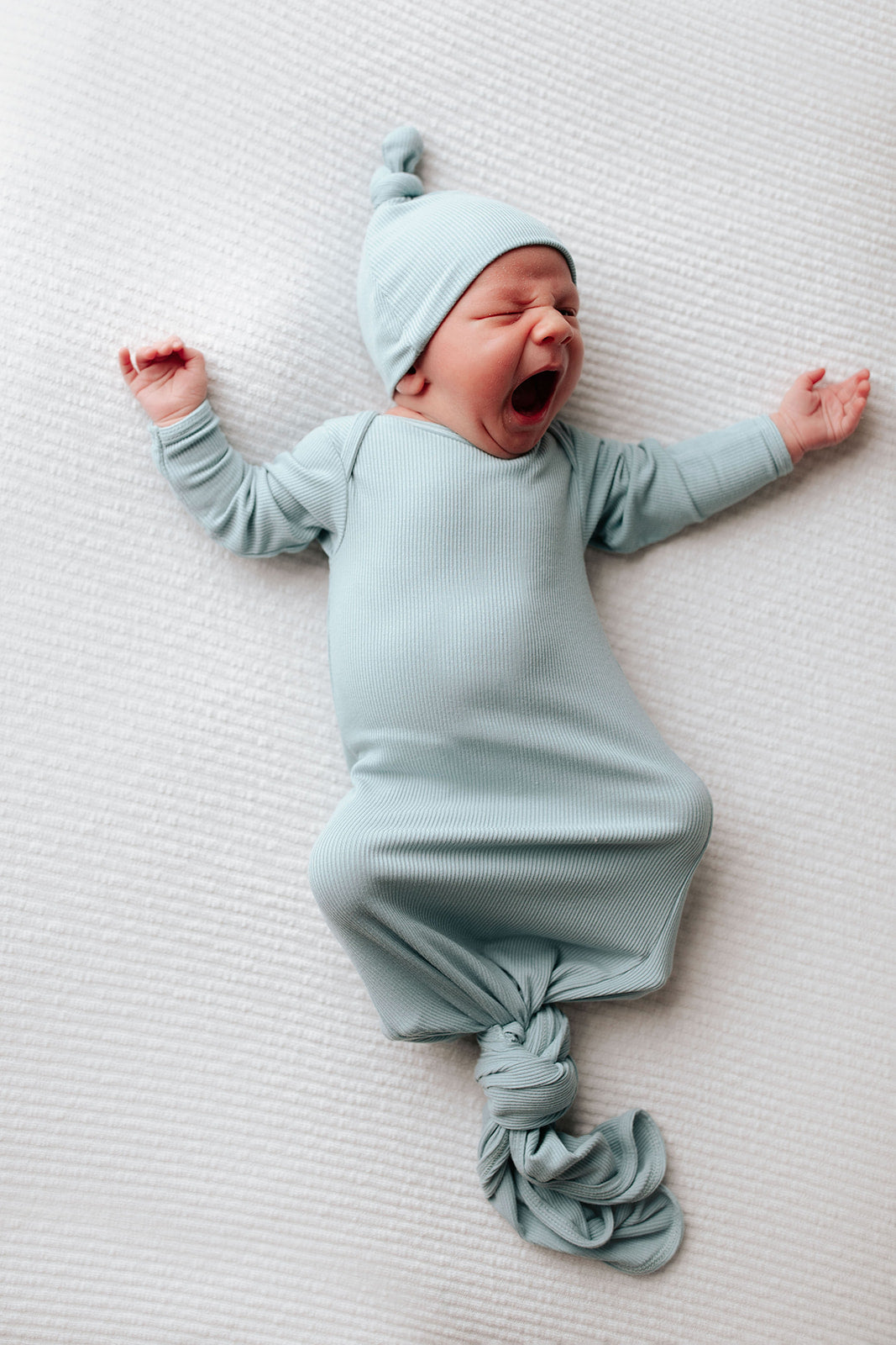 newborn baby in a blue knotted gown with a newborn baby yawning