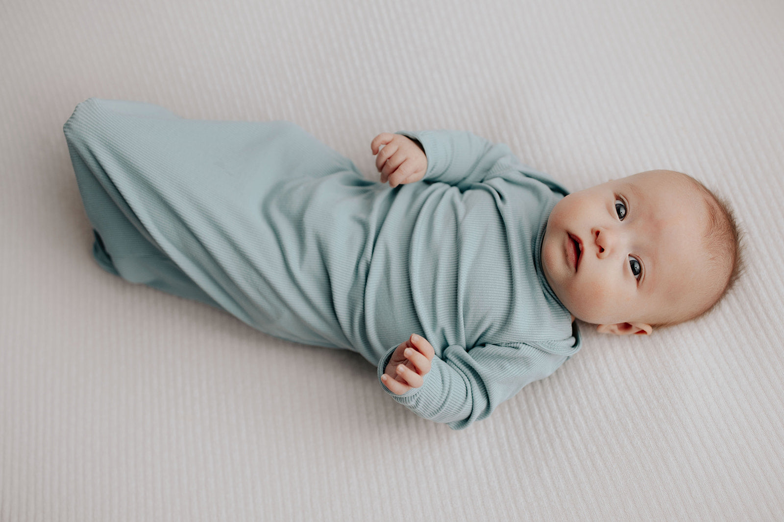 newborn baby in a Three Little Tots knotted gown stretching newborn foot out.